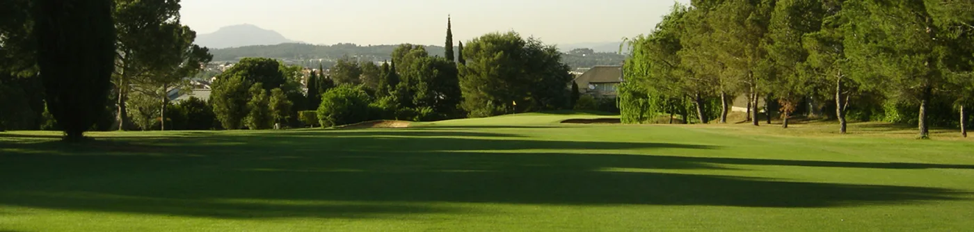 A fairway running downhill at Club de Golf Sant Cugat, framed by cypress and pine with the hills beyond