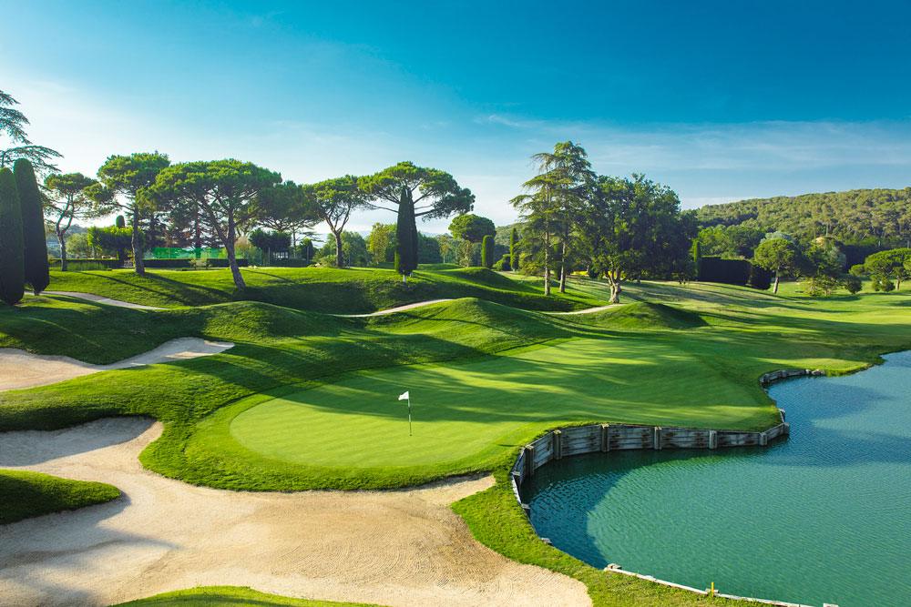 A green at Club de Golf Vallromanes guarded by bunkers and a lake, with umbrella pines behind