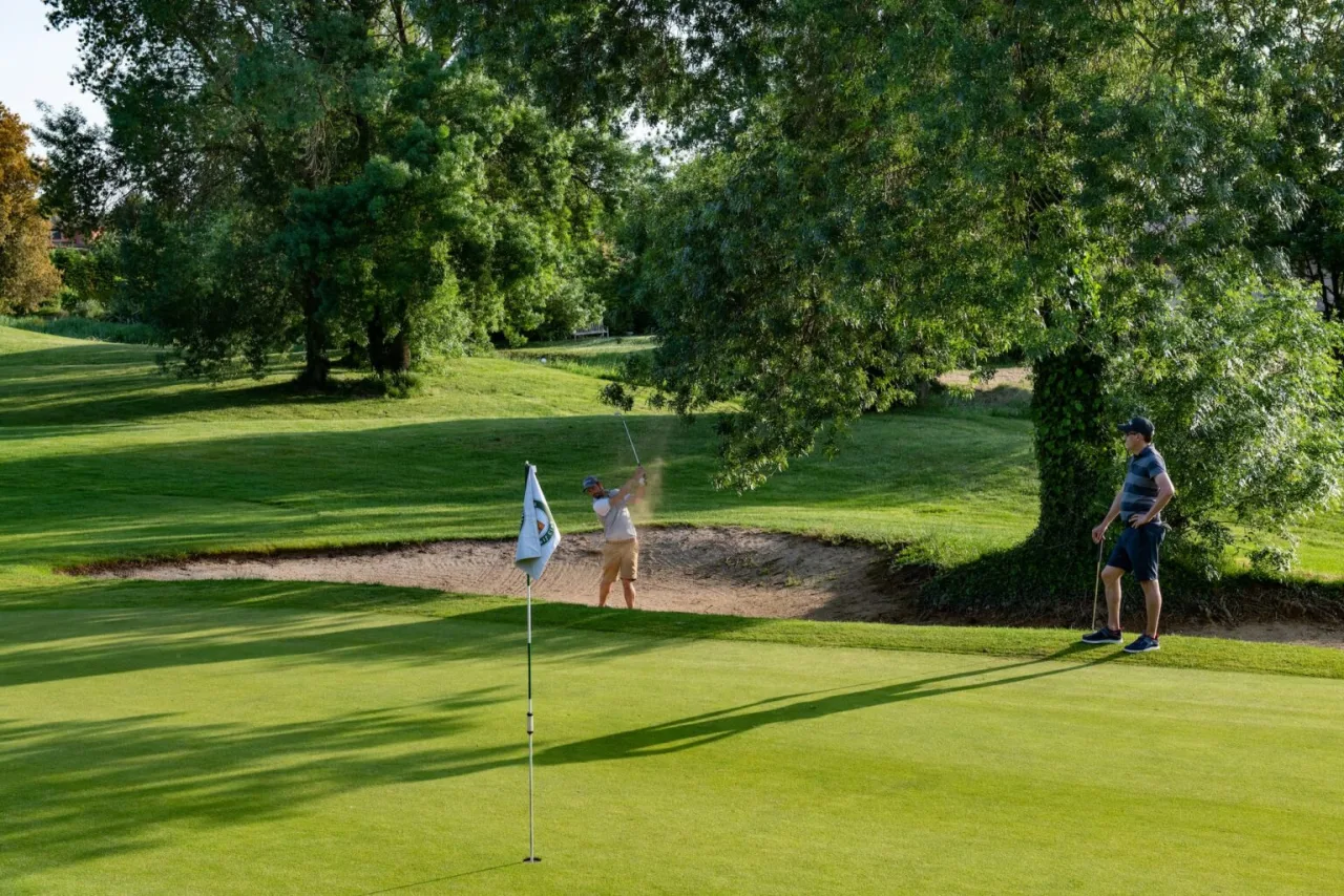 A green at Torremirona Golf Club with a bunker and mature trees, players finishing the hole