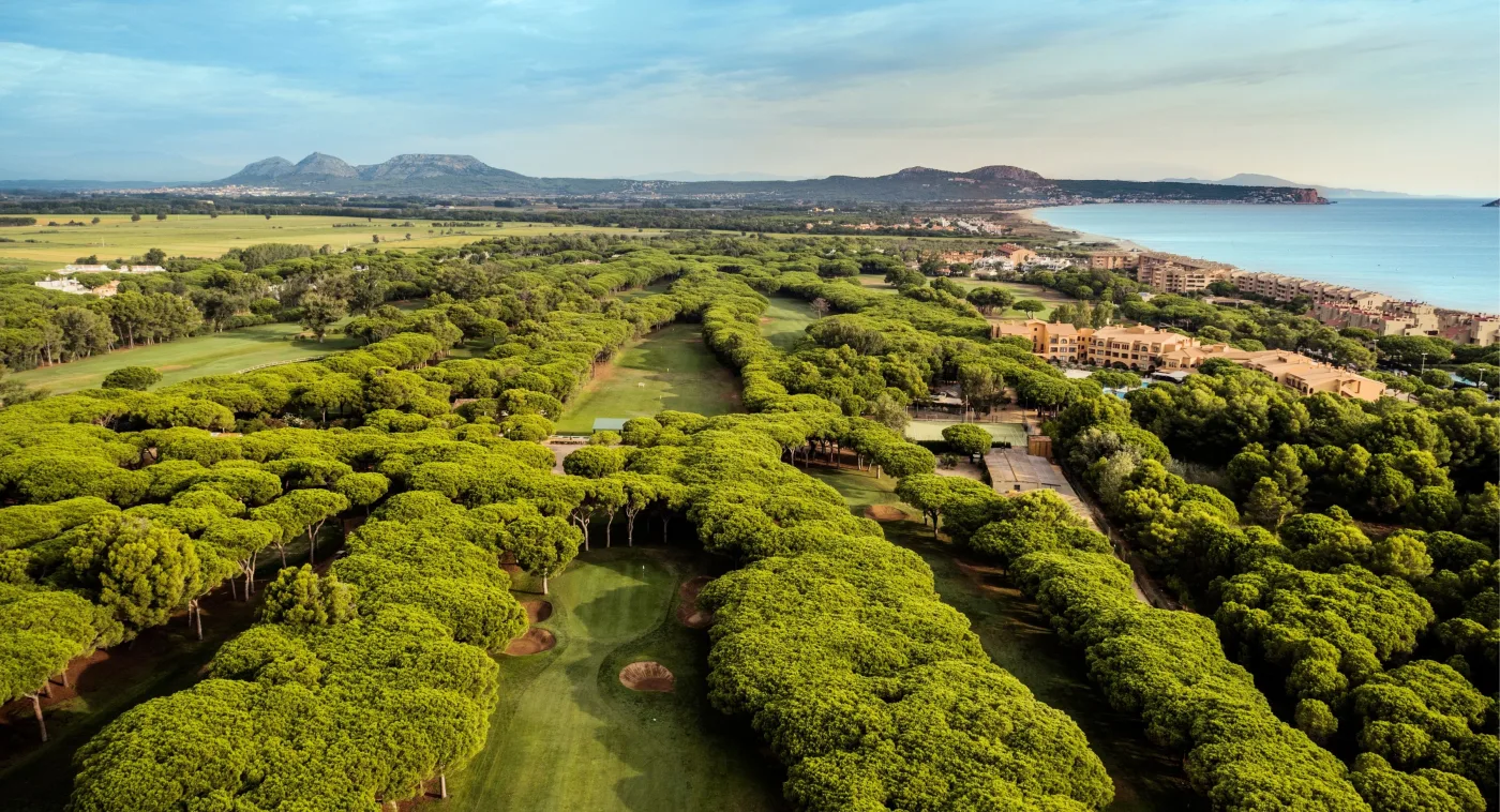 Aerial view of Golf de Pals, its fairways cut through umbrella pine forest with the Costa Brava coast beyond