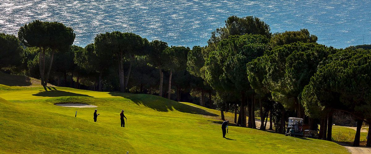 A fairway and green at Golf Sant Vicen&ccedil; de Montalt, with umbrella pines and the Mediterranean behind